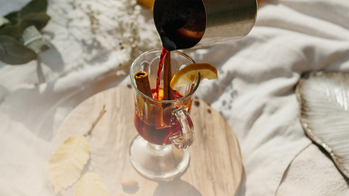 Glas Kombucha Orangen Punsch Kanne giesst ein Zimtstange Holzbrett Tuch
